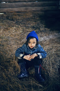 Village boy a child in boots is sitting
on the hay in a barn in warm clothes and a blue hat