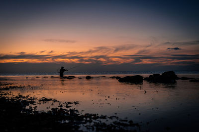 Silhouette person on beach against sky during sunset