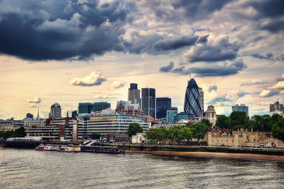 Modern buildings by river against sky in city