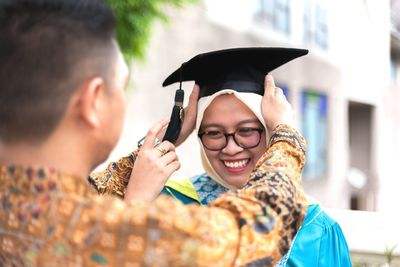 Man putting mortarboard on cheerful student