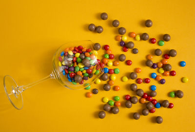 Colorful candies in a wine glass on yellow background