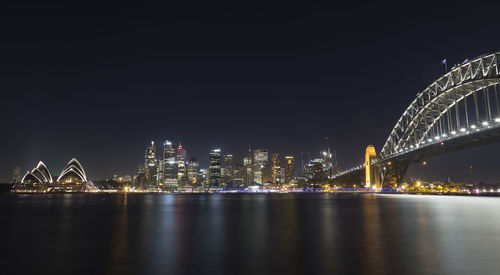 Illuminated sydney harbour bridge and opera house by bay against clear sky