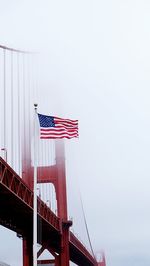 Low angle view of flag waving by bridge against sky during foggy weather