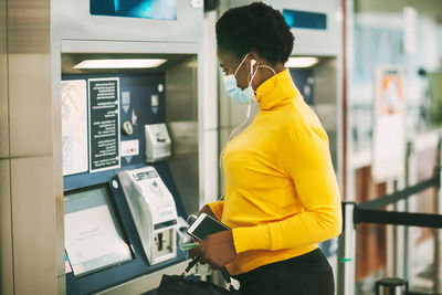 Dubai, uae, november 2020 african woman wearing a protective mask withdraws money from a bank card