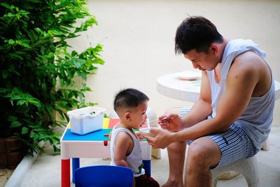 Father feeding son while sitting against wall