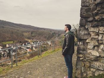 Side view of man standing against stone wall while looking at townscape