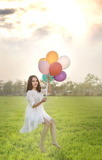 Full length of woman holding balloons on field against sky