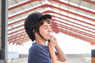 Adolescent boy putting a riding helmet on his head.