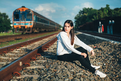 Young woman looking away sitting by railroad tracks