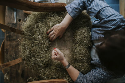 High angle view of female upholsterer making chair with straws while standing in workshop