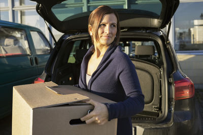 Businesswoman carrying cardboard box in front of car trunk