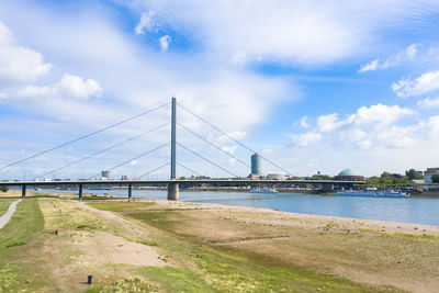 View of suspension bridge over river against cloudy sky