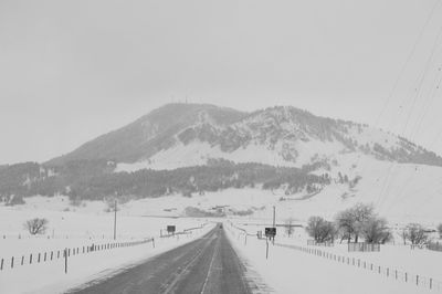 Road by mountains against clear sky during winter