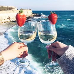 Close-up of hand holding wineglass against sea