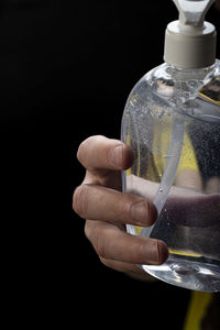 Close-up of hand holding glass bottle against black background