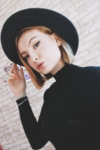 Portrait of young woman wearing hat standing against wall