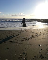 Silhouette boy standing on beach against sky during sunset