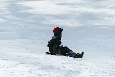 Side view of boy tobogganing on snow