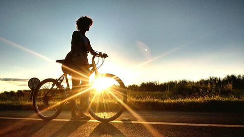 Silhouette woman riding bicycle on road at sunset