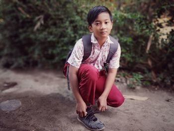 Portrait of boy tying shoelace while crouching against plants