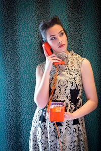 Young woman looking away while talking on phone against wall