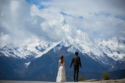 Couple standing in front of snowcapped mountains against cloudy sky