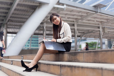 Portrait of businesswoman writing while sitting against office building