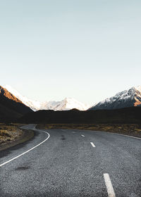 Road leading towards mountains against clear sky