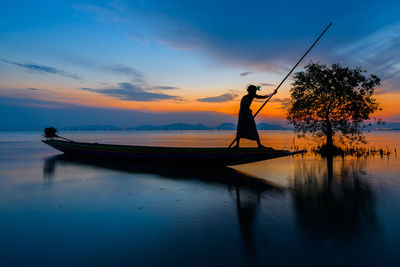 Silhouette man fishing in lake against sky during sunset