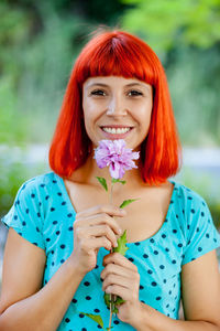 Portrait of smiling woman holding flower standing outdoors