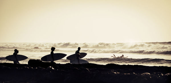 Silhouette people with surfboards at beach against sky