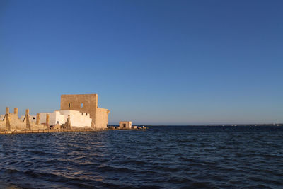 Scenic view of sea by buildings against clear blue sky