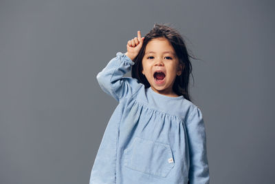 Cute girl with mouth open gesturing against gray background