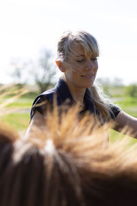 Smiling woman standing by horse on field during sunny day