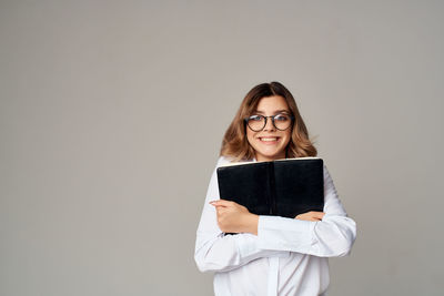 Portrait of young woman holding book against gray background