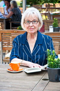 Portrait of senior woman reading book while sitting at cafe