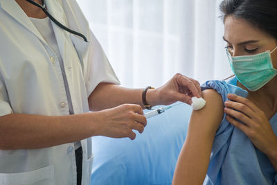 Midsection of doctor injecting patient on table