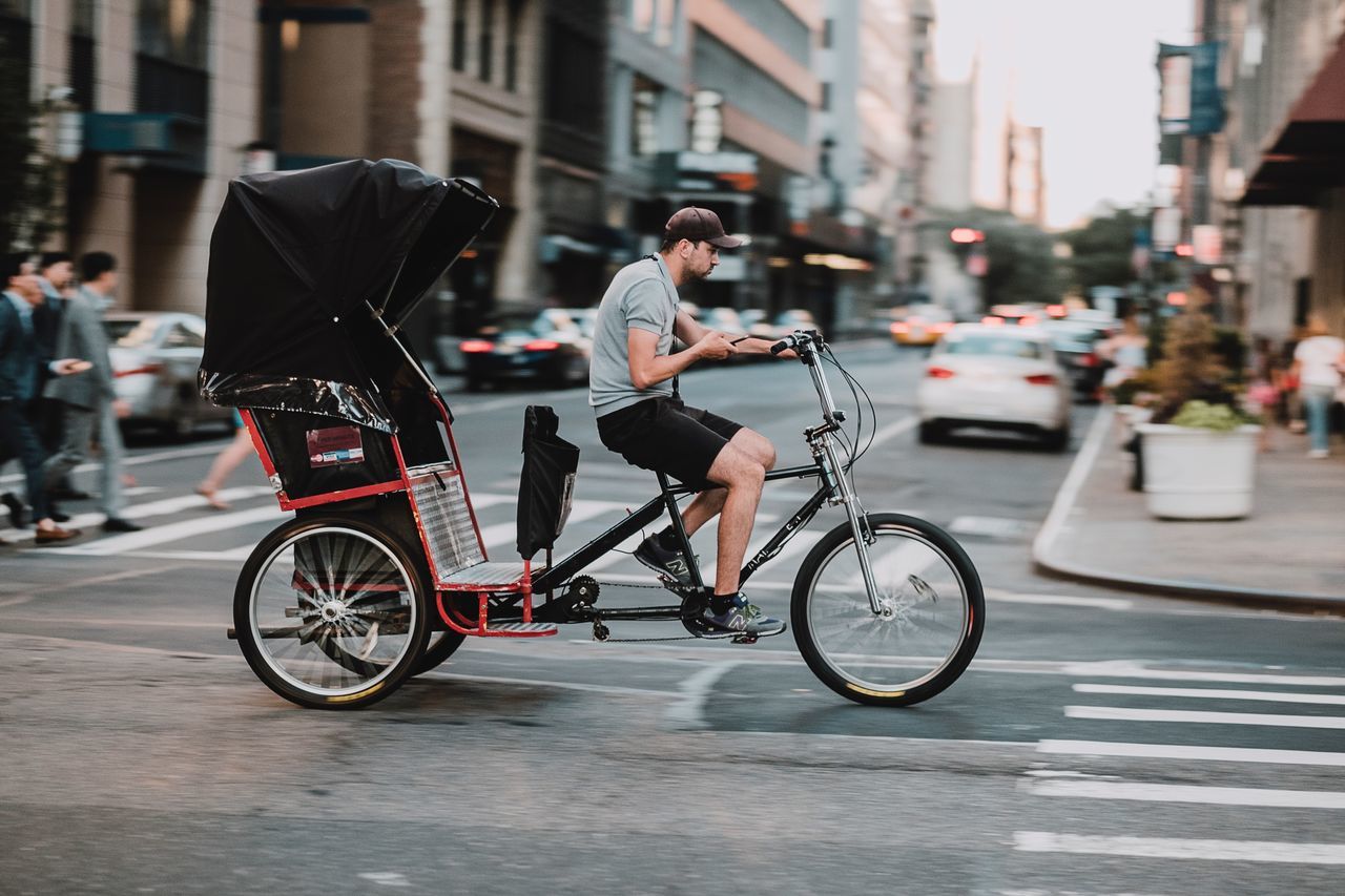 city, transportation, street, bicycle, mode of transportation, real people, architecture, full length, building exterior, land vehicle, lifestyles, one person, riding, ride, city street, city life, incidental people, focus on foreground, men, road, outdoors