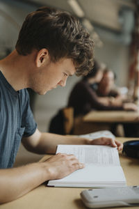 Male student reading book in library at university