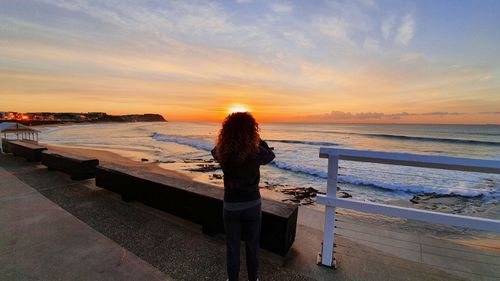 Rear view of woman looking at sea during sunset