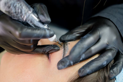Eyebrow microblading. a master in black gloves holds a blending needle over the brow of the model.