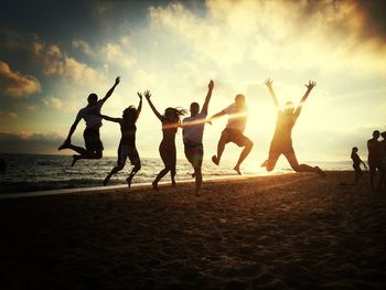 People at beach against sky during sunset