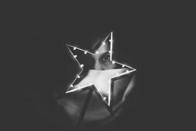 Portrait of woman looking through star shaped illuminated light in darkroom