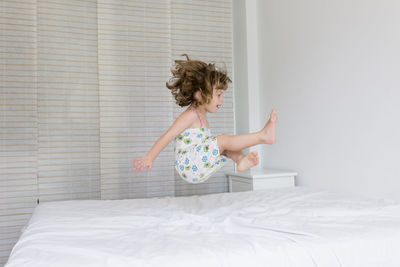 Side view of girl jumping on bed at home