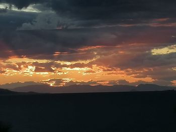 Silhouette landscape against dramatic sky during sunset