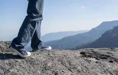 Low section of man walking on mountain against sky
