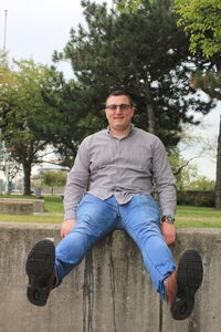 Portrait of young man sitting on plant against trees