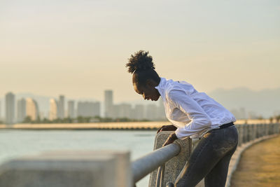 Side view of young woman in city against sky