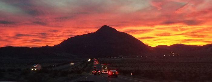 Cars on road against dramatic sky during sunset