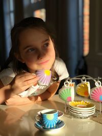 Cute girl looking away holding coffee cup sitting by table at home